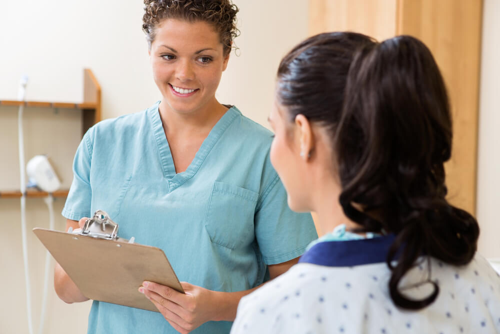 Happy mid adult nurse with clipboard looking at patient