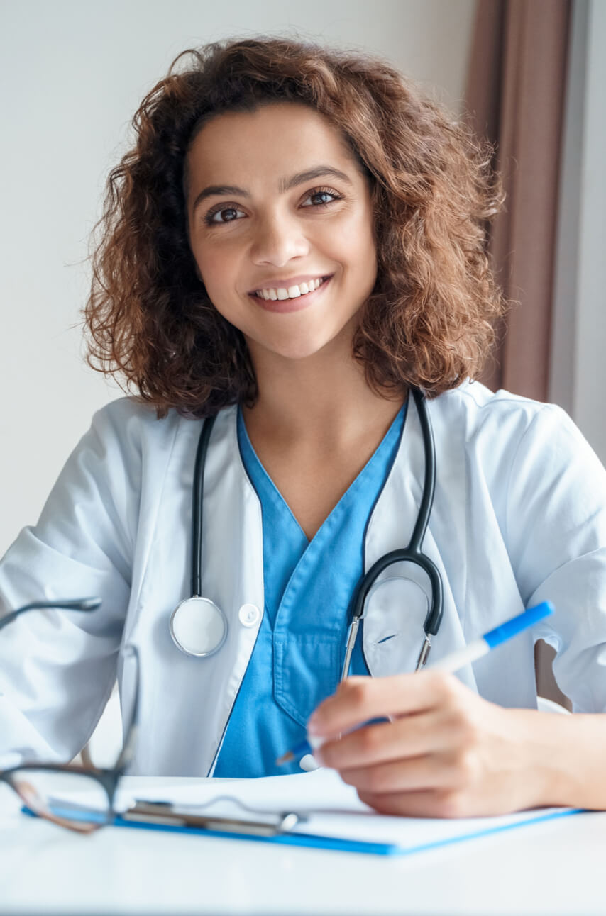 Female doctor sitting on work desk and smiling at camera